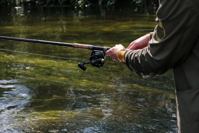 A person enjoying fishing on a calm river with a rod and reel, showcasing leisure activity