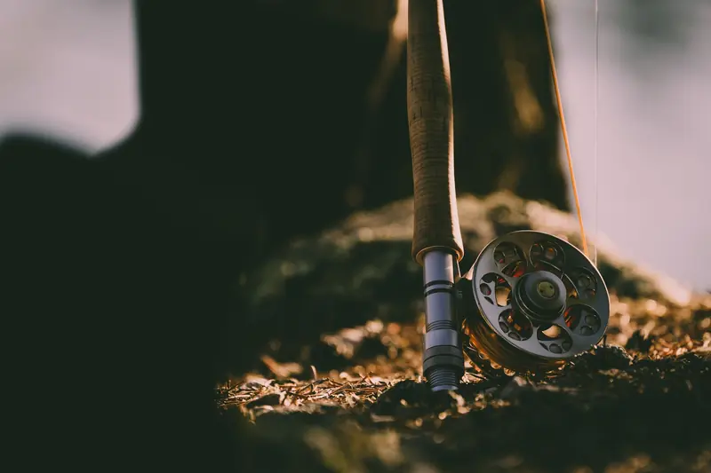 Detailed close-up of a vintage-style fishing rod and reel resting on autumn ground; a serene outdoor scene