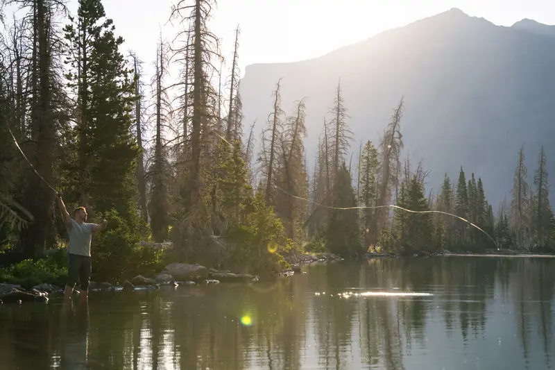 A lone fly fisherman casting his line in a tranquil mountain lake during daylight